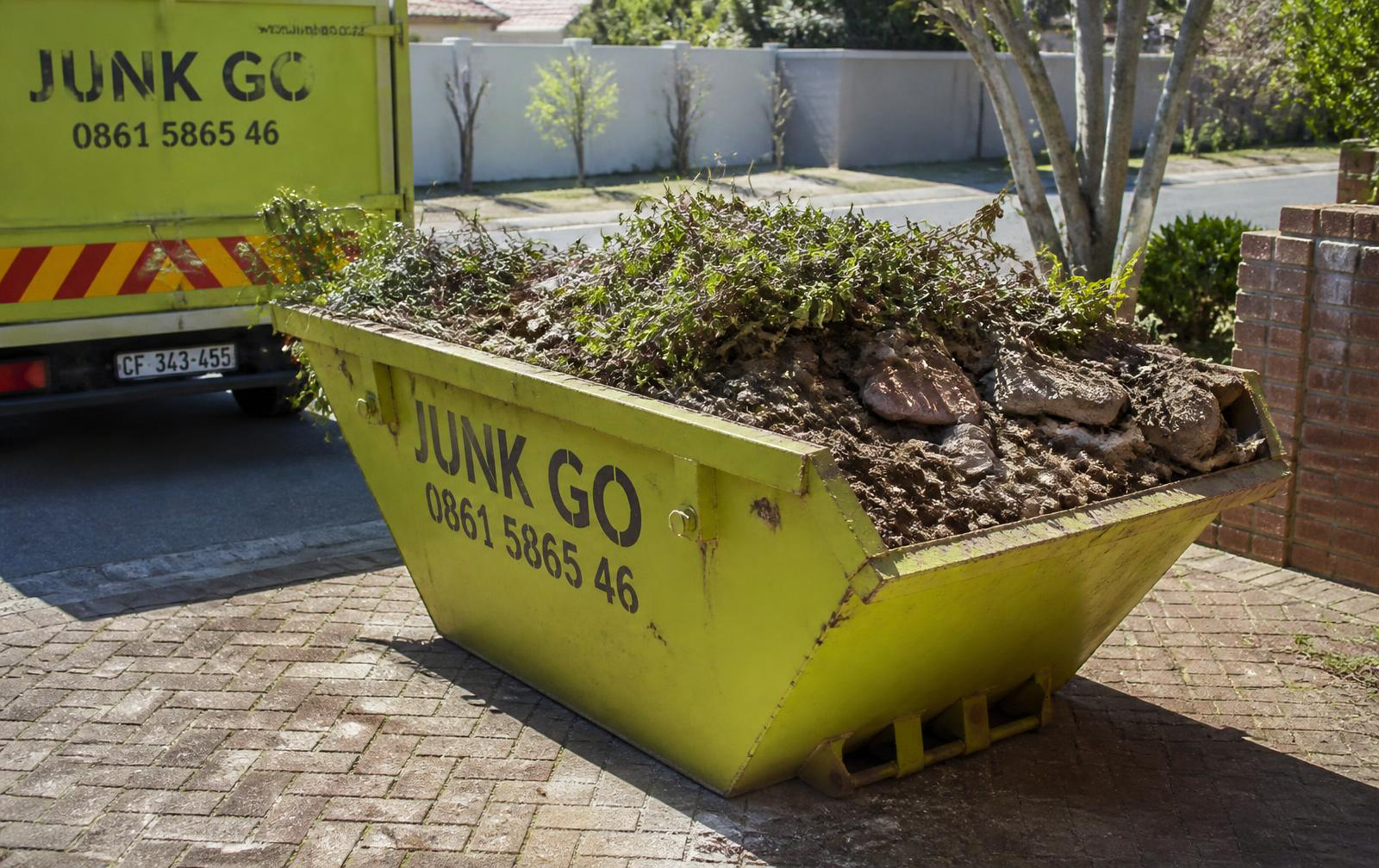 Bright lime-green skip bin filled with garden refuse and rubble on a residential driveway